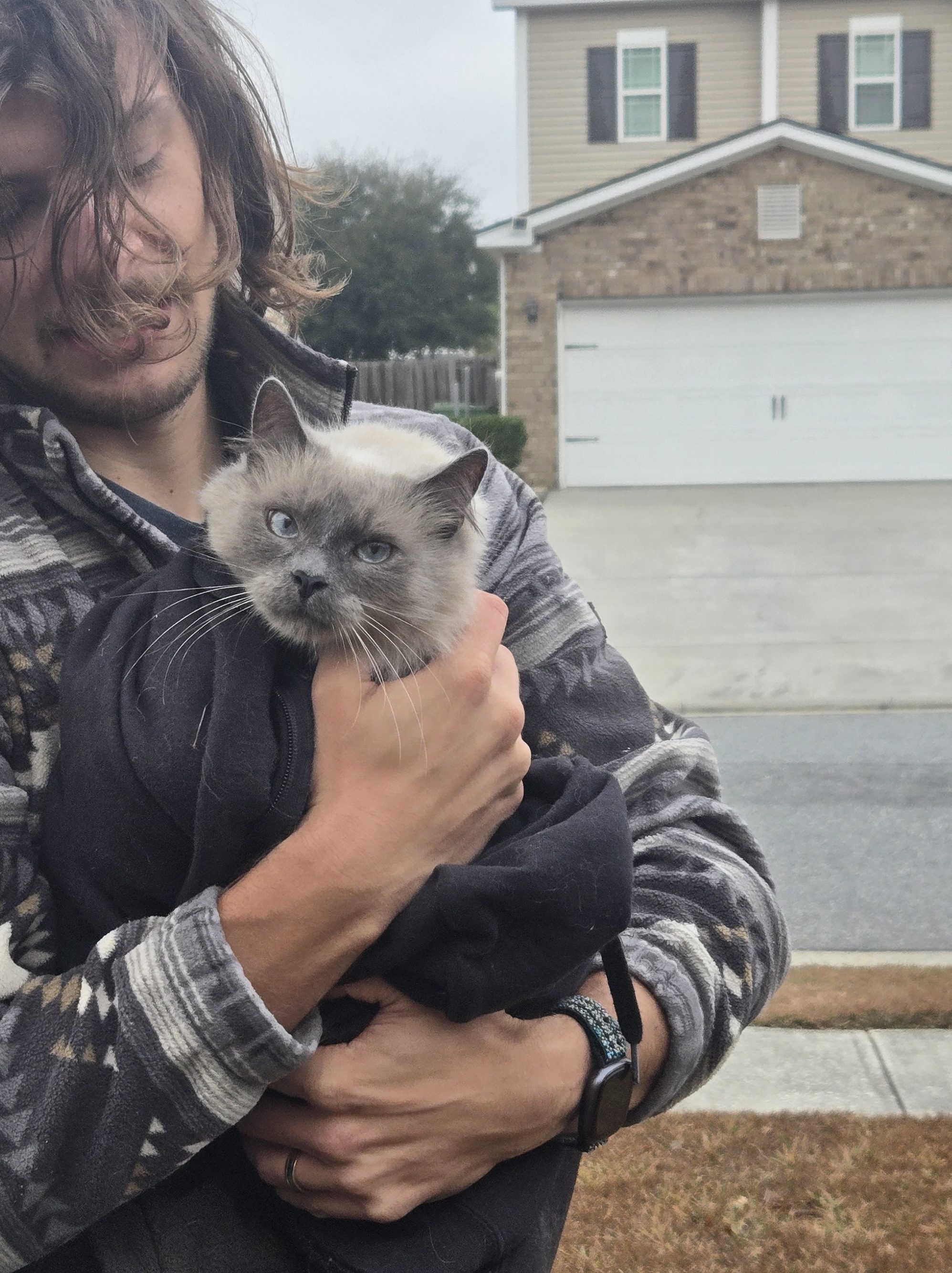 Ethan holding Goose wrapped in a black hoodie after rescuing him from under a car